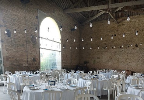 Salle de réception en pierre dressée avec nappes blanches et guirlandes lumineuses